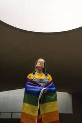 Junge Frau stehend mit Regenbogenflagge - MGRF00301