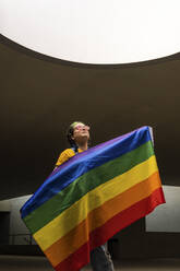 Junge Hipster-Frau hält Regenbogenflagge - MGRF00302