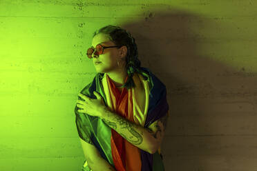 Woman with LGBTQIA flag looking away while standing by wall - MGRF00308