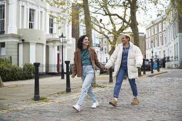 Glückliches lesbisches Paar, das sich die Hände hält, während es gemeinsam auf dem Fußweg spazieren geht - PMF01899