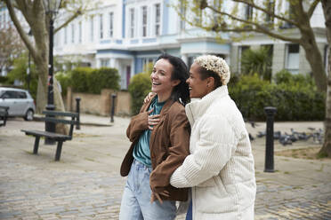 Cheerful lesbian couple wearing jacket standing together on footpath - PMF01901