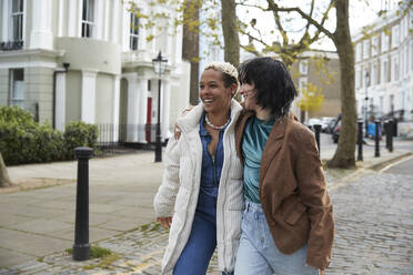 Glückliches lesbisches Paar, das auf dem Gehweg spazieren geht und sich umarmt - PMF01904