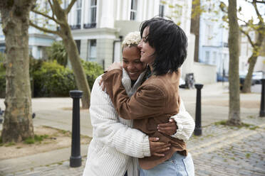 Glückliches lesbisches Paar, das sich umarmt und auf dem Fußweg steht - PMF01905