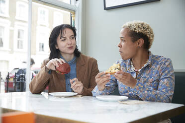 Lesbian couple eating fast food while sitting at table in cafe - PMF01916