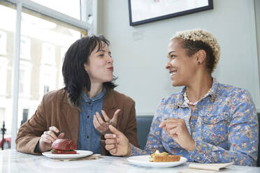 Happy lesbian couple eating fast food sitting together in cafe - PMF01918