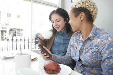 Frau teilt Smartphone mit Freundin beim Kaffeetrinken im Café - PMF01921