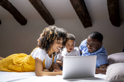 Smiling family using laptop with son while lying on bed at home - OCMF02161