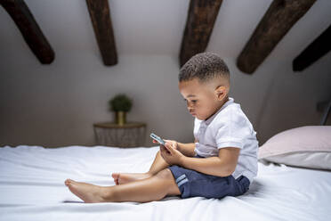 Junge benutzt Smartphone, während er zu Hause auf dem Bett sitzt - OCMF02180