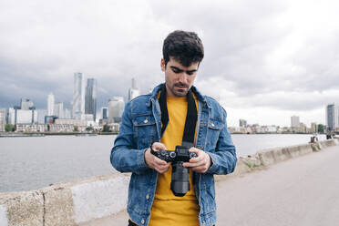 Young man checking camera while standing on promenade - ASGF00683