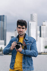 Handsome young man in denim jacket using camera - ASGF00685