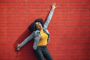 Glückliche junge Frau lehnt an einer roten Backsteinmauer - JSRF01572