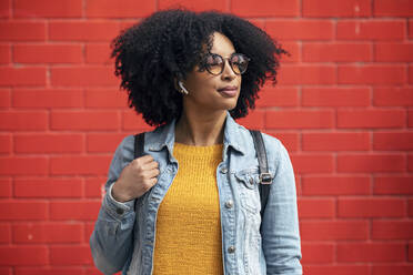 Thoughtful young woman looking away in front of red wall - JSRF01574