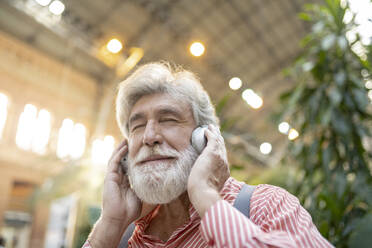 Weißer, bärtiger, reifer Mann mit geschlossenen Augen hört Musik über eine drahtlose Kopfhörerstation - JCCMF02985