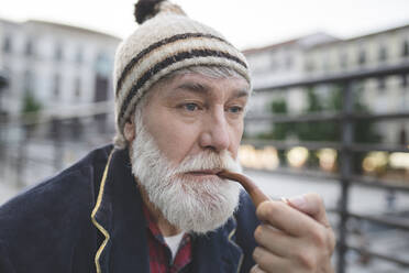 Nachdenklicher reifer Mann mit weißem Bart und Strickmütze raucht Pfeife - JCCMF03032