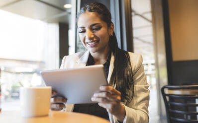 Geschäftsfrau lächelt bei der Nutzung eines digitalen Tablets in einem Café - JCCMF03035