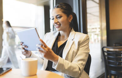 Smiling businesswoman using digital tablet while sitting in coffee shop - JCCMF03036