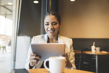 Weibliche Fachkraft, die im Café sitzend ein digitales Tablet benutzt - JCCMF03037