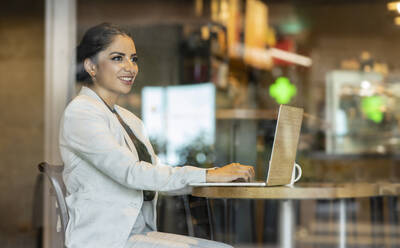 Lächelnde Geschäftsfrau mit Laptop in einem Café sitzend - JCCMF03043