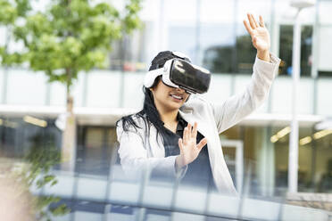 Geschäftsfrau, die ihre Hände ausstreckt, während sie ein Virtual-Reality-Headset benutzt - JCCMF03060