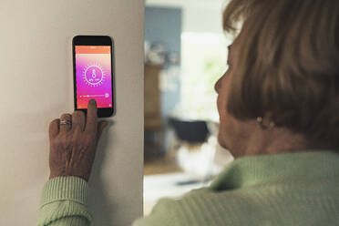 Ältere Frau steuert die Raumtemperatur über ein Hausautomatisierungsgerät - UUF23650