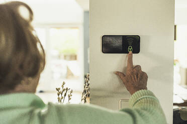 Senior woman unlocking home automation device on wall - UUF23656