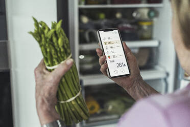 Woman calculating food calories through smart phone at home - UUF23659