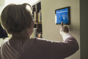 Senior woman using futuristic smart home device on wall - UUF23671