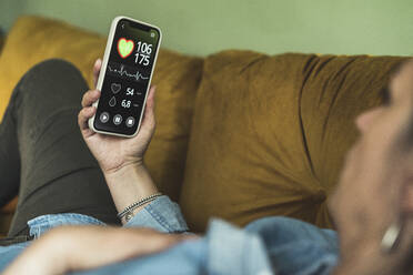 Woman examining pulse trace record through smart phone at home - UUF23695