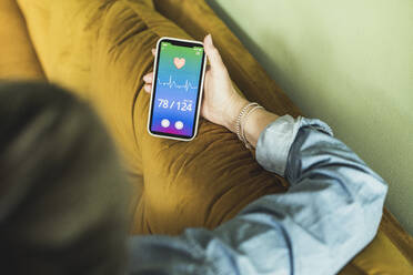 Woman checking pulse trace medical record through smart phone at home - UUF23697