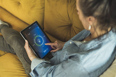 Frau stellt den Timer über ein digitales Tablet ein, während sie zu Hause auf dem Sofa sitzt - UUF23698