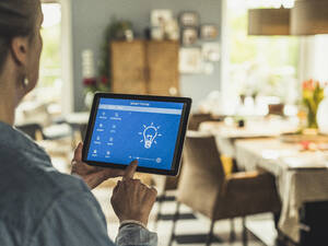 Woman operating home automation device through digital tablet at home - UUF23705