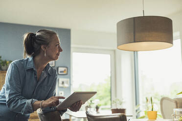 Reife Frau, die mit einem digitalen Tablet zu Hause die Beleuchtung einschaltet - UUF23710