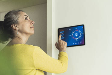 Woman looking away while standing by home automation device on wall - UUF23714