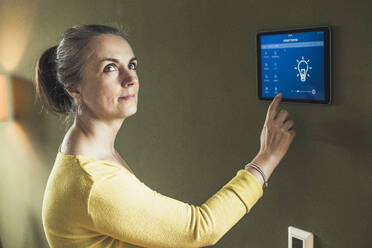 Woman using futuristic smart home device on wall - UUF23717