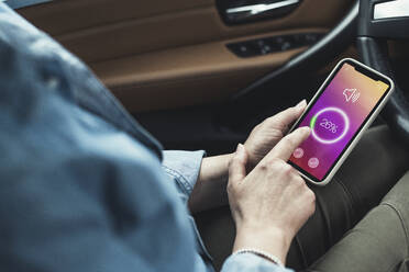 Woman adjusting volume through smart phone while sitting in car - UUF23724