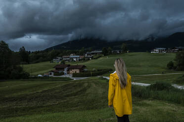 Frau in gelbem Regenmantel steht auf Gras unter dramatischem Himmel - AKLF00278