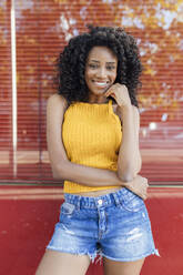 Smiling young woman standing in front of red window - JRVF01168