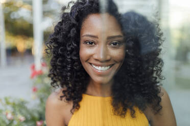 Smiling curly haired woman seen through glass wall - JRVF01183