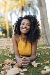 Smiling curly haired woman lying on grass at park - JRVF01191