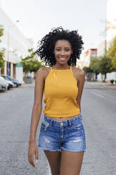 Smiling curly haired woman walking on street - JRVF01198