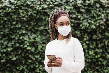 Young woman wearing protective face mask holding smart phone - NMSF00437