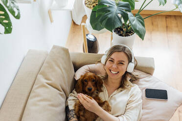 Happy woman with Cocker Spaniel relaxing on sofa in living room - VPIF04187