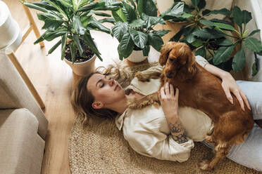 Young woman with Cocker Spaniel lying on rug at home - VPIF04193