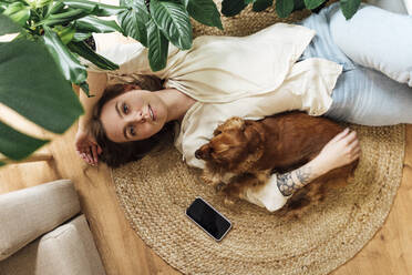 Beautiful woman with dog lying on rug at home - VPIF04194
