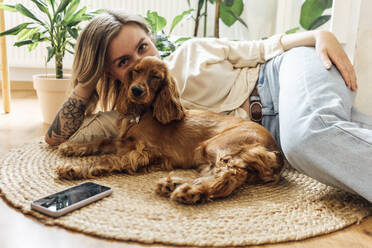 Young woman with dog relaxing on rug at home - VPIF04195