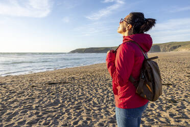 Frau mit Rucksack genießt die Einsamkeit am Strand bei Sonnenuntergang - WPEF04920