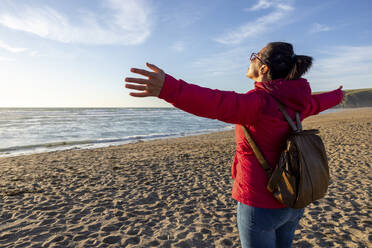 Carefree woman standing with arms outstretched at beach - WPEF04921