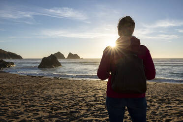 Frau mit Rucksack bei Sonnenuntergang am Strand stehend - WPEF04922