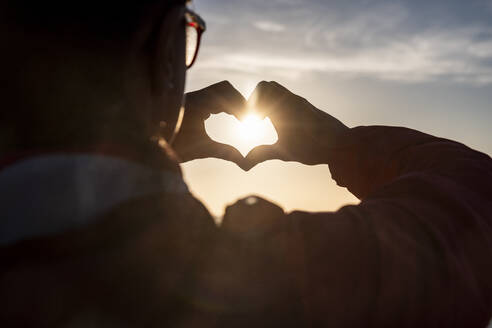 Frau macht Herzform mit Händen während Sonnenuntergang - WPEF04923