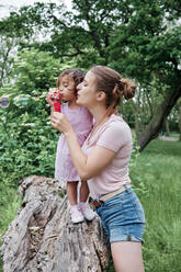 Mother and daughter blowing bubbles in park - ASGF00690